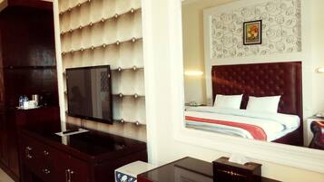 Habitación de hotel con una cama grande, televisión, minibar y un espejo que refleja la decoración de la habitación.