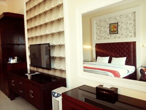 A hotel room with a large bed, a television, a minibar, and a mirror reflecting the room's decor. - Grand City Batu Hotel (Batu)