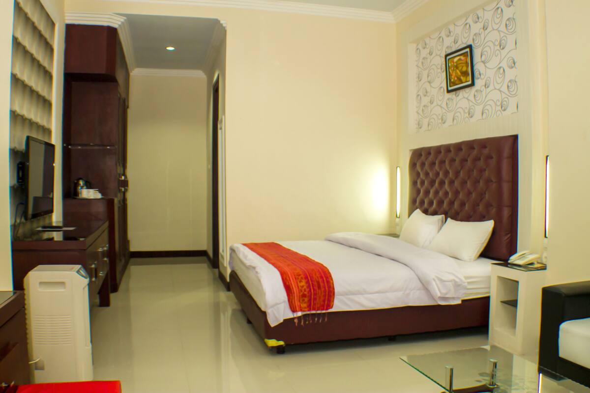 A hotel room with a large bed, a television, a desk, and a glass coffee table.