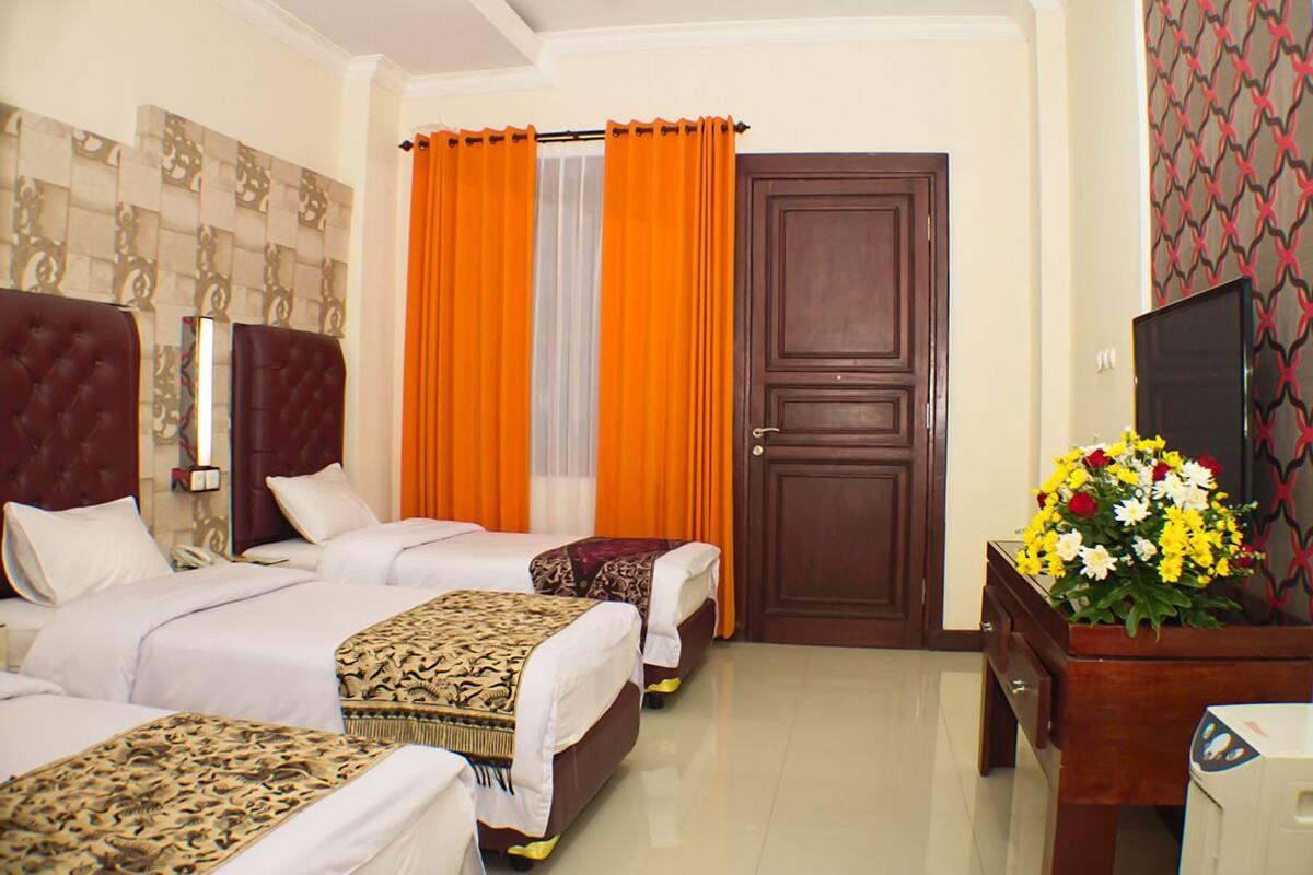 A hotel room with two beds, a wooden door, a TV, and a flower vase.