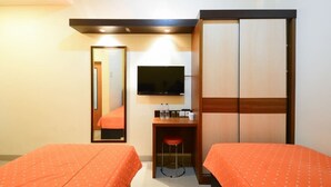 A hotel room with two beds, a TV, a wardrobe, a desk with a chair, and a mirror. - My Residence Cirebon (West Cirebon)