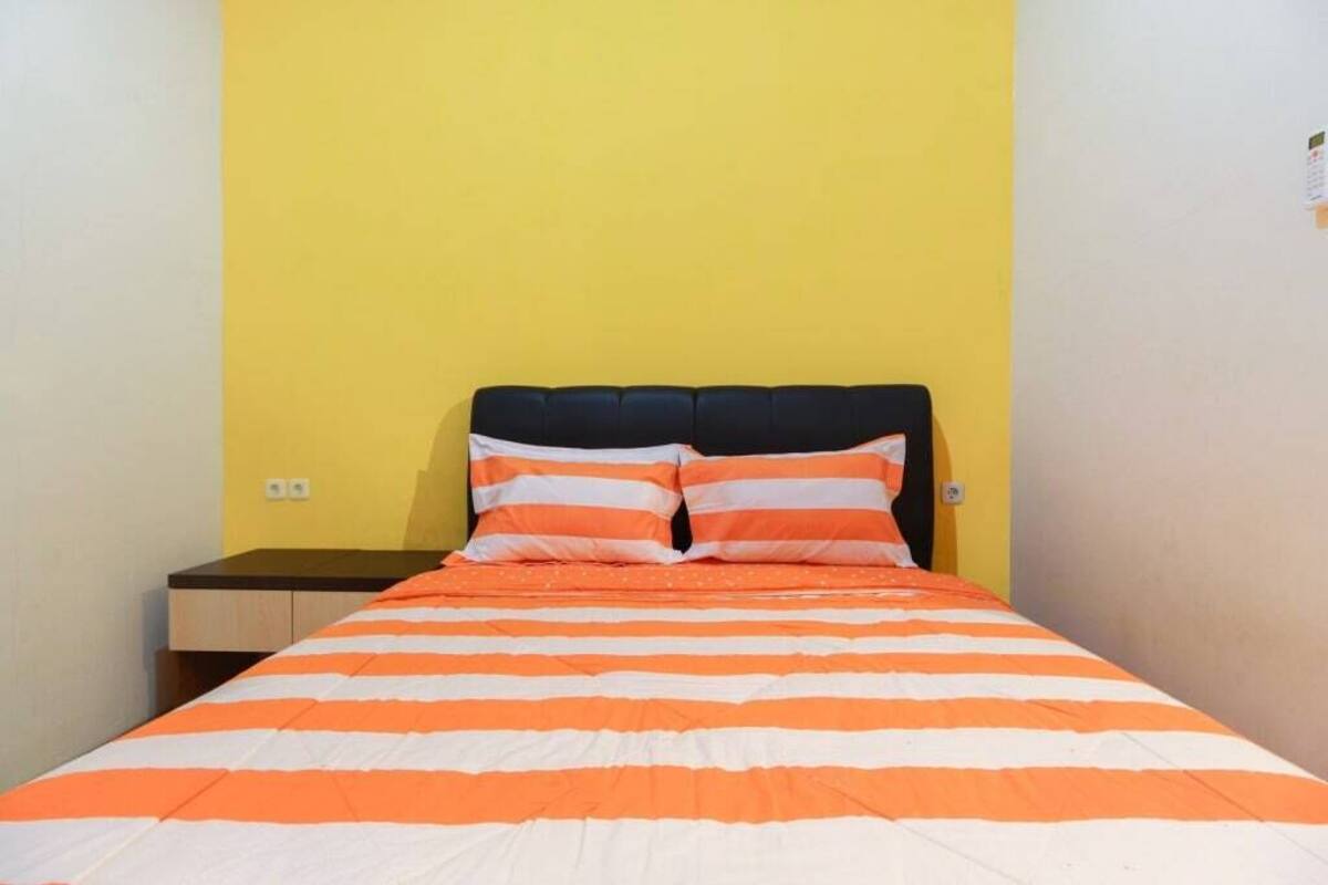 Un lit avec une couvre-lit rayée orange et blanche et des coussins assortis, placé devant un mur jaune.
