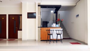 A hotel reception area with a reception desk, two chairs, and a staircase leading to the upper floors. - My Residence Cirebon (West Cirebon)