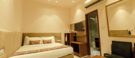 A hotel room with a bed, a desk, a chair, a TV, a mirror, and an air conditioning unit.