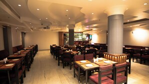 A restaurant with multiple dining tables and chairs, a bar area, and a large pillar. - Jullundur Hotel (Chandigarh)