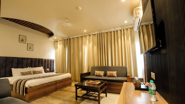 A hotel room with a bed, sofa, coffee table, TV, and a bottle of water. - Jullundur Hotel (Chandigarh)