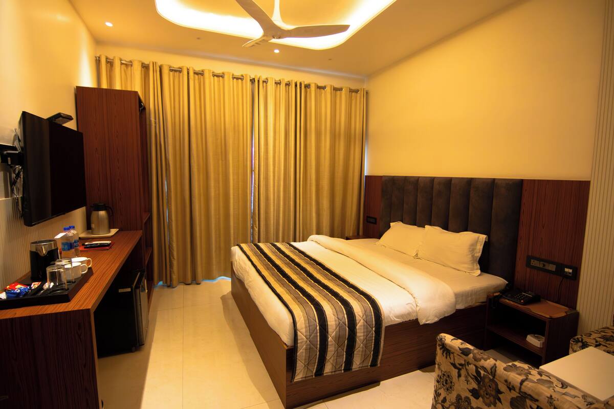 Een hotelkamer met een groot bed, een bureau met een flatscreen televisie, een koffiezetapparaat en een klein nachtkastje met een lamp.