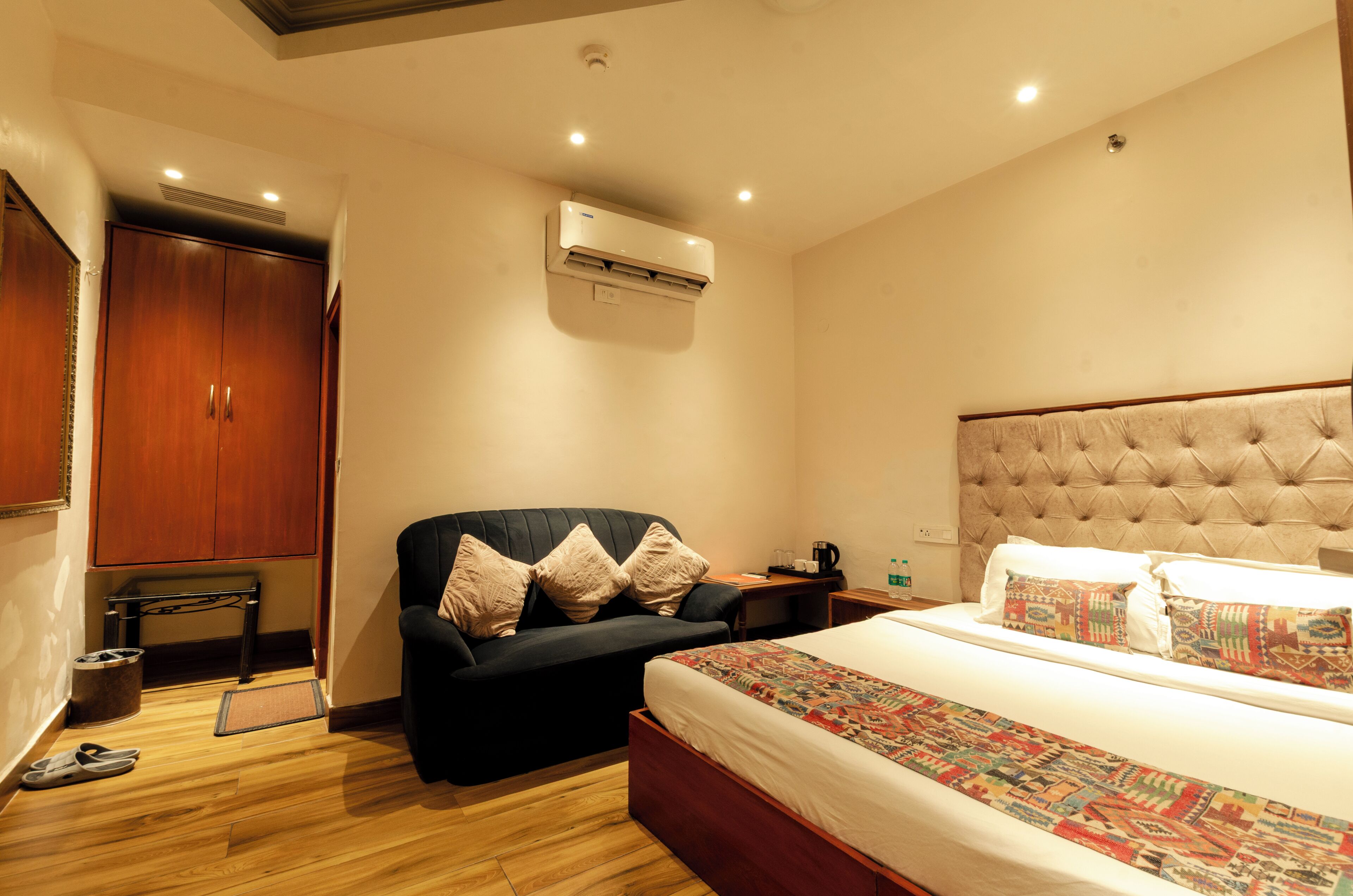 Habitación de hotel con cama, sofá, aire acondicionado, armario y mesita de noche.