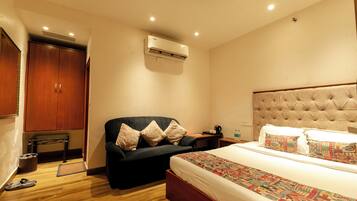 Habitación de hotel con cama, sofá, aire acondicionado, armario y mesita de noche.