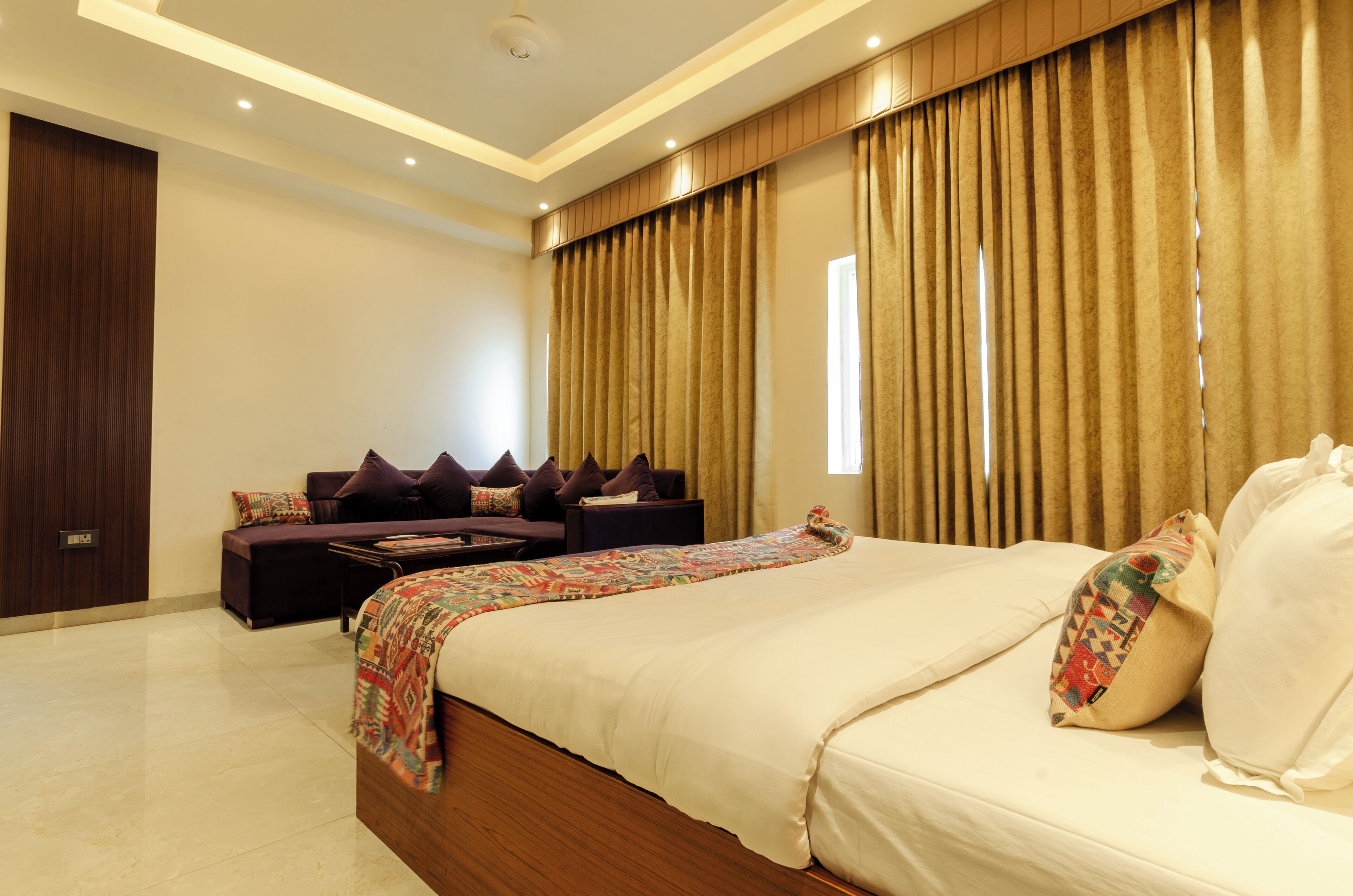 A modern bedroom with a large bed, a sofa, and a window with curtains.