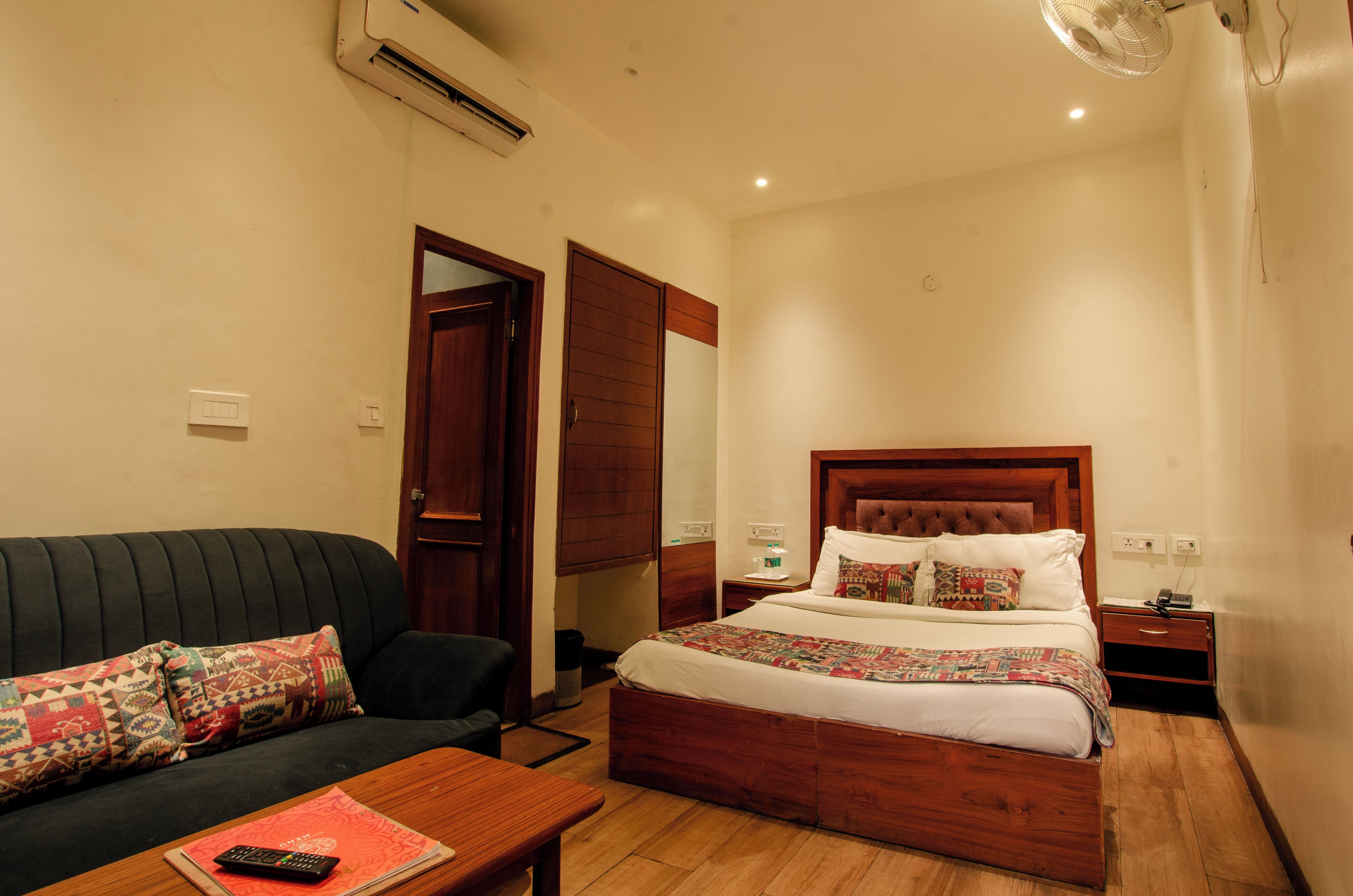 Een slaapkamer met een bed, een houten hoofdbord, een nachtkastje, een bijzettafeltje, een stoel, een bank en een wandairconditioner.