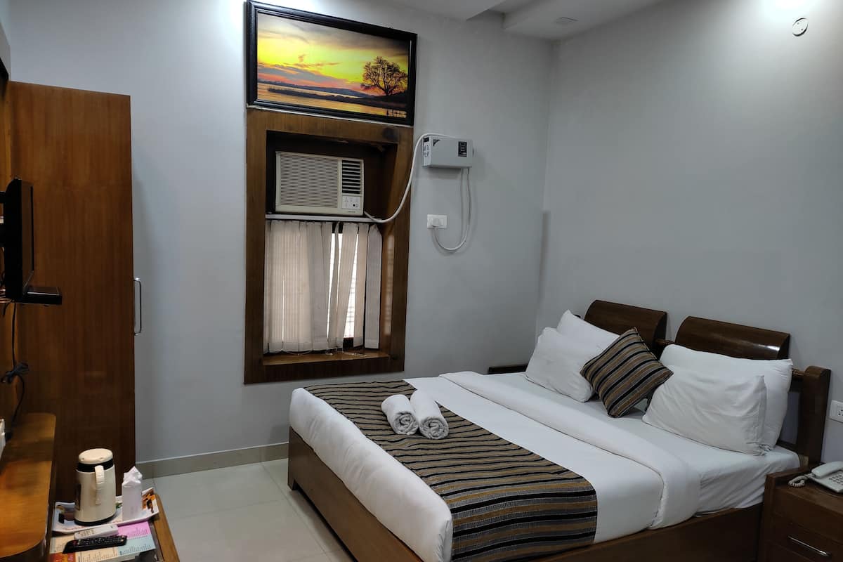 A hotel room with a bed, a wooden desk with a coffee maker, a telephone, and a painting above the window.