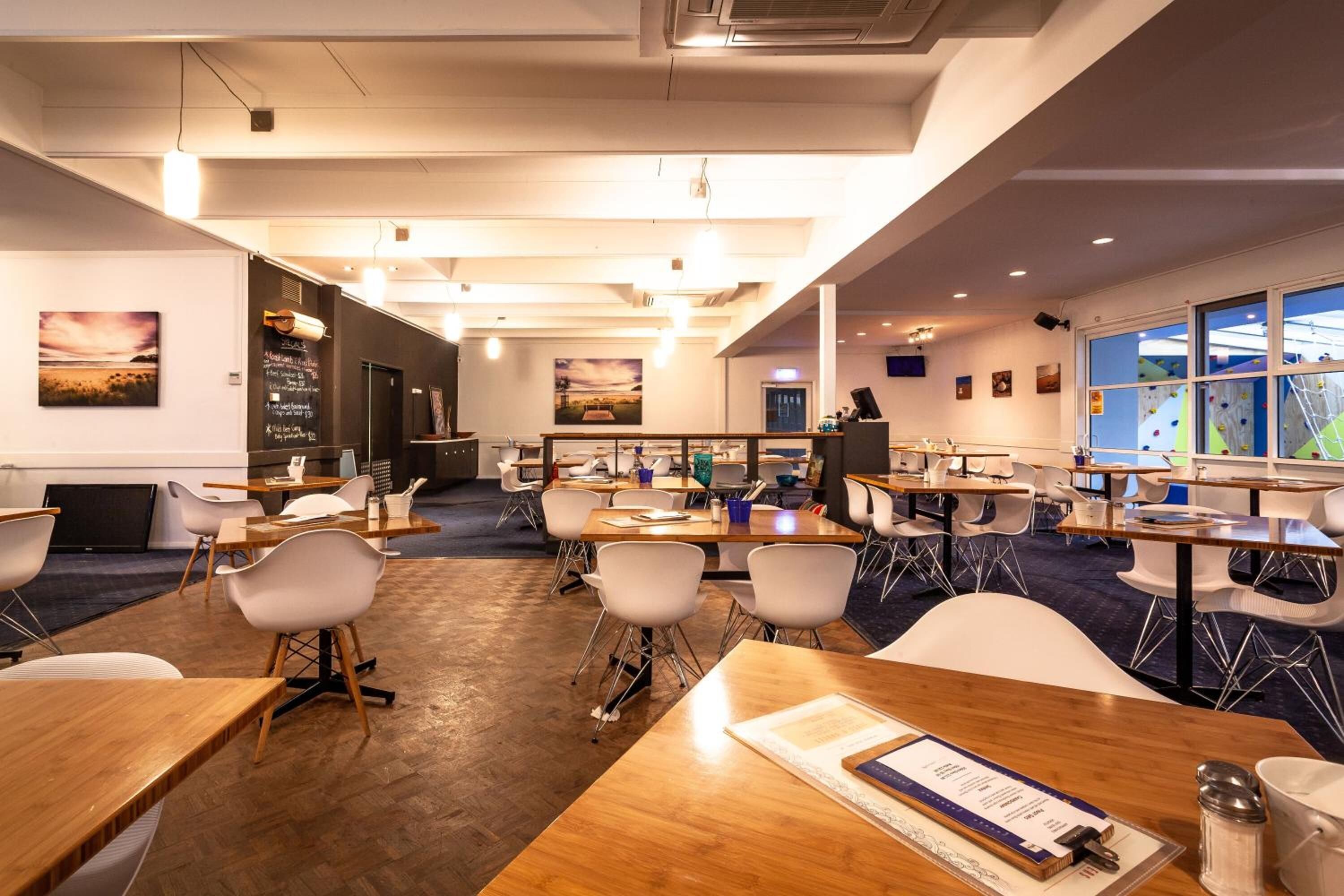 A modern conference room with wooden tables and white chairs, equipped with presentation screens and a large window offering a view of the outdoors.