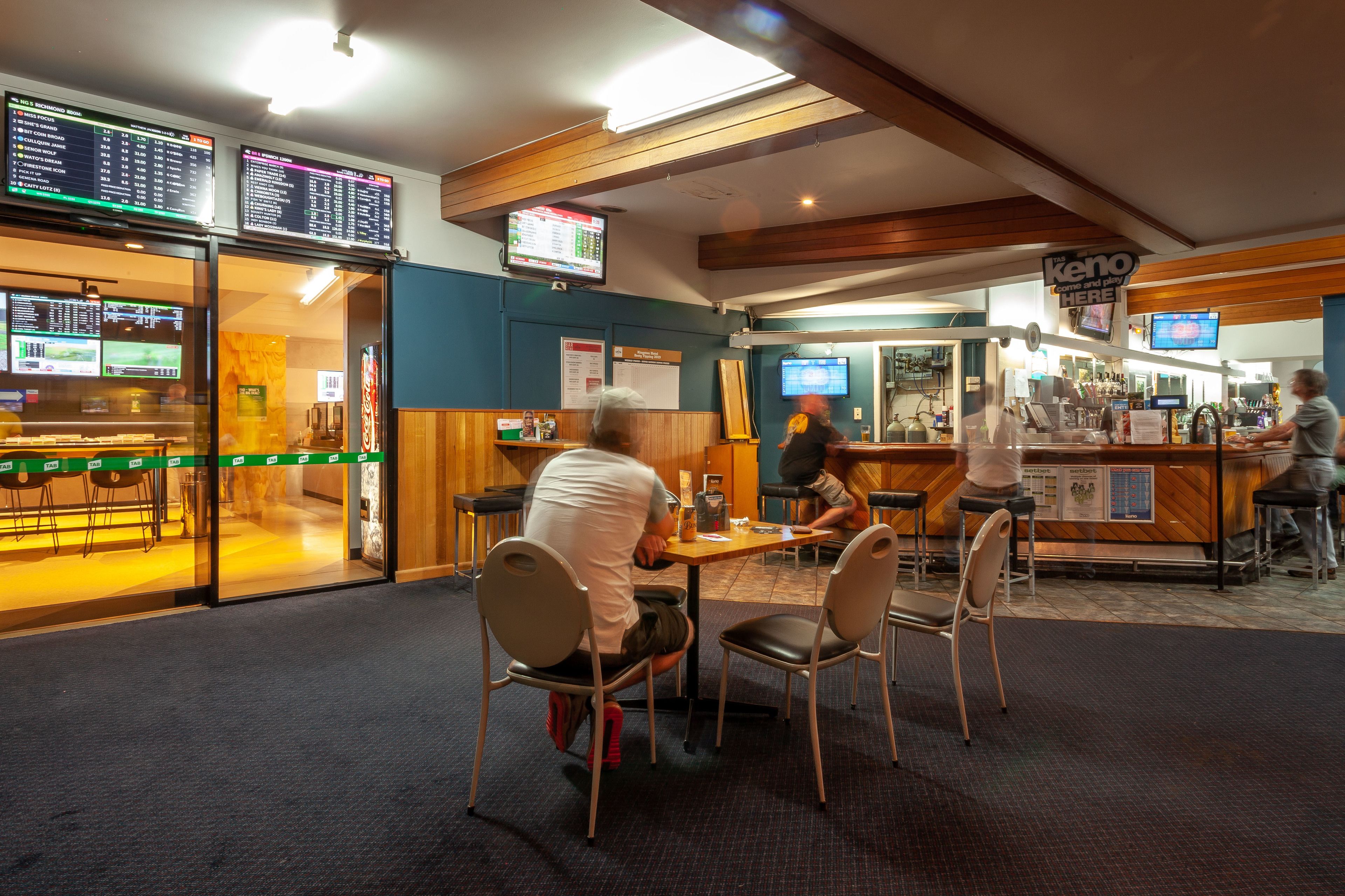 A restaurant with a bar area, multiple screens displaying menus and information, and a counter with a person serving.