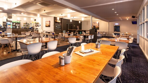 A spacious conference room with multiple tables and chairs, a reception area, and a bar. - Kingston Hotel (Kingston)