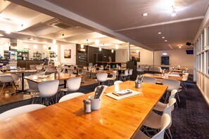 A spacious conference room with multiple tables and chairs, a reception area, and a bar. - Kingston Hotel (Kingston)