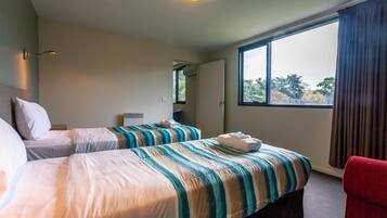 A hotel room with two beds, a red chair, and a large window with a view of trees.