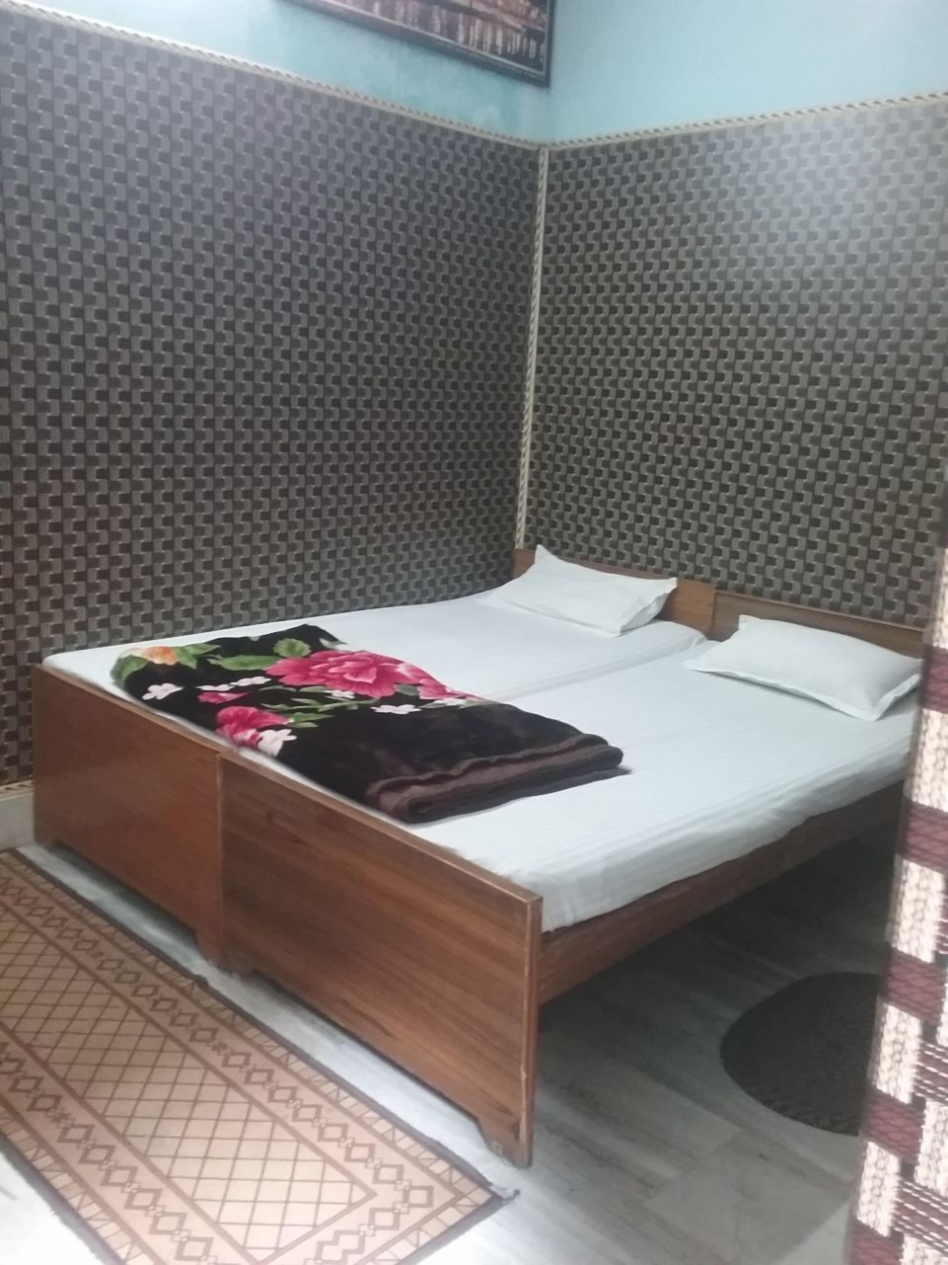 A bedroom with a bed, a wooden nightstand, a patterned rug, and acoustic panels on the walls.