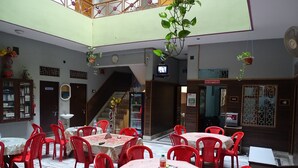 Un restaurante con varias mesas, sillas rojas, una escalera y una zona de recepción.