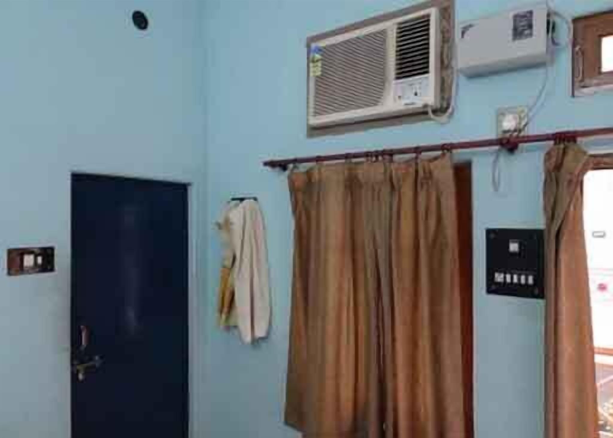 A room with light blue walls, a door, an air conditioning unit, and a curtain rod with a single curtain.