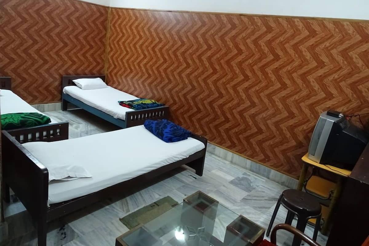 A room with two single beds, a glass-top table, a television, and a wooden herringbone-patterned wall.