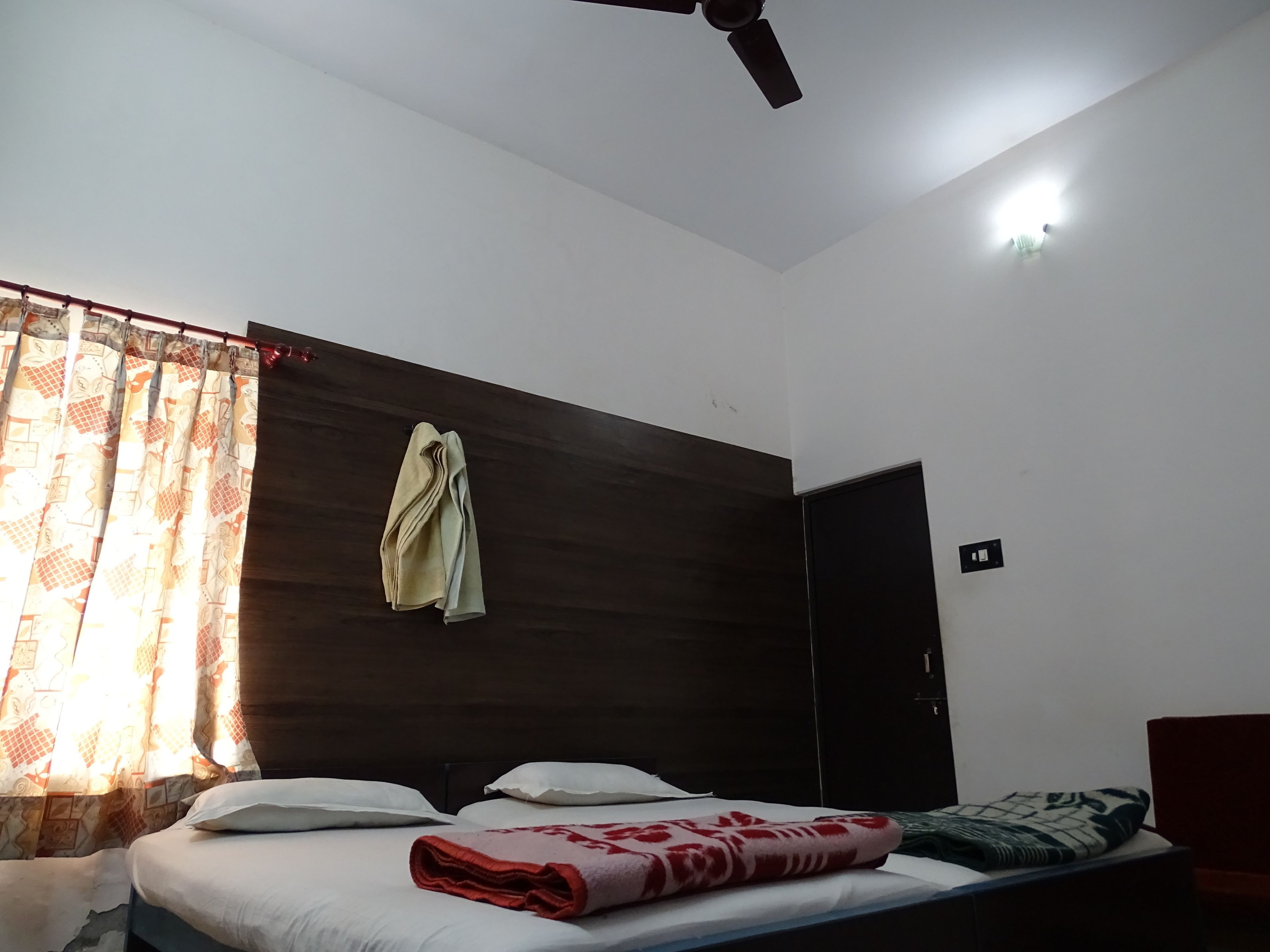 A bedroom with a bed, a ceiling fan, a window with curtains, and a door.