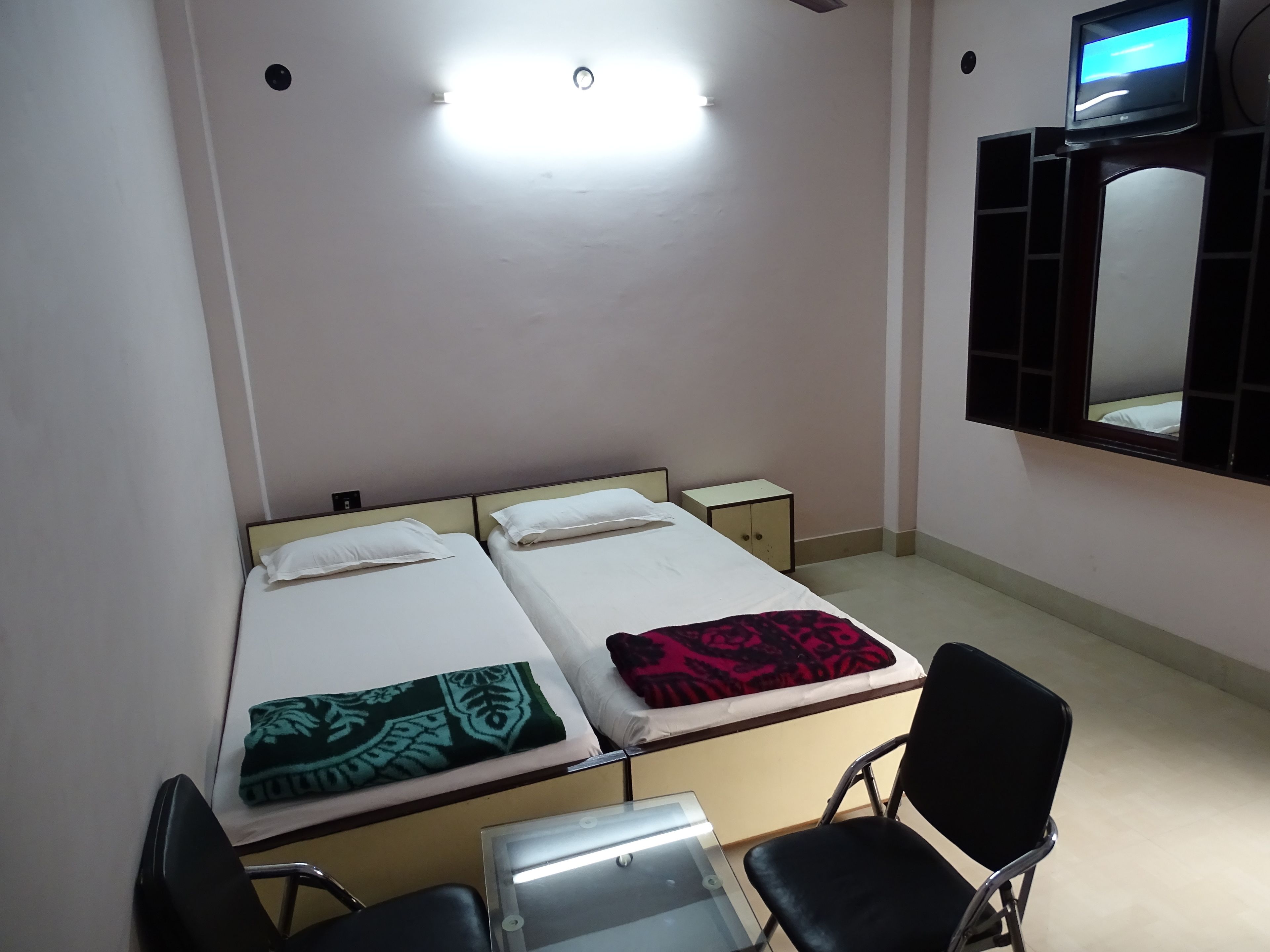 A room with two single beds, a small table, a chair, a TV on the wall, and a mirror.
