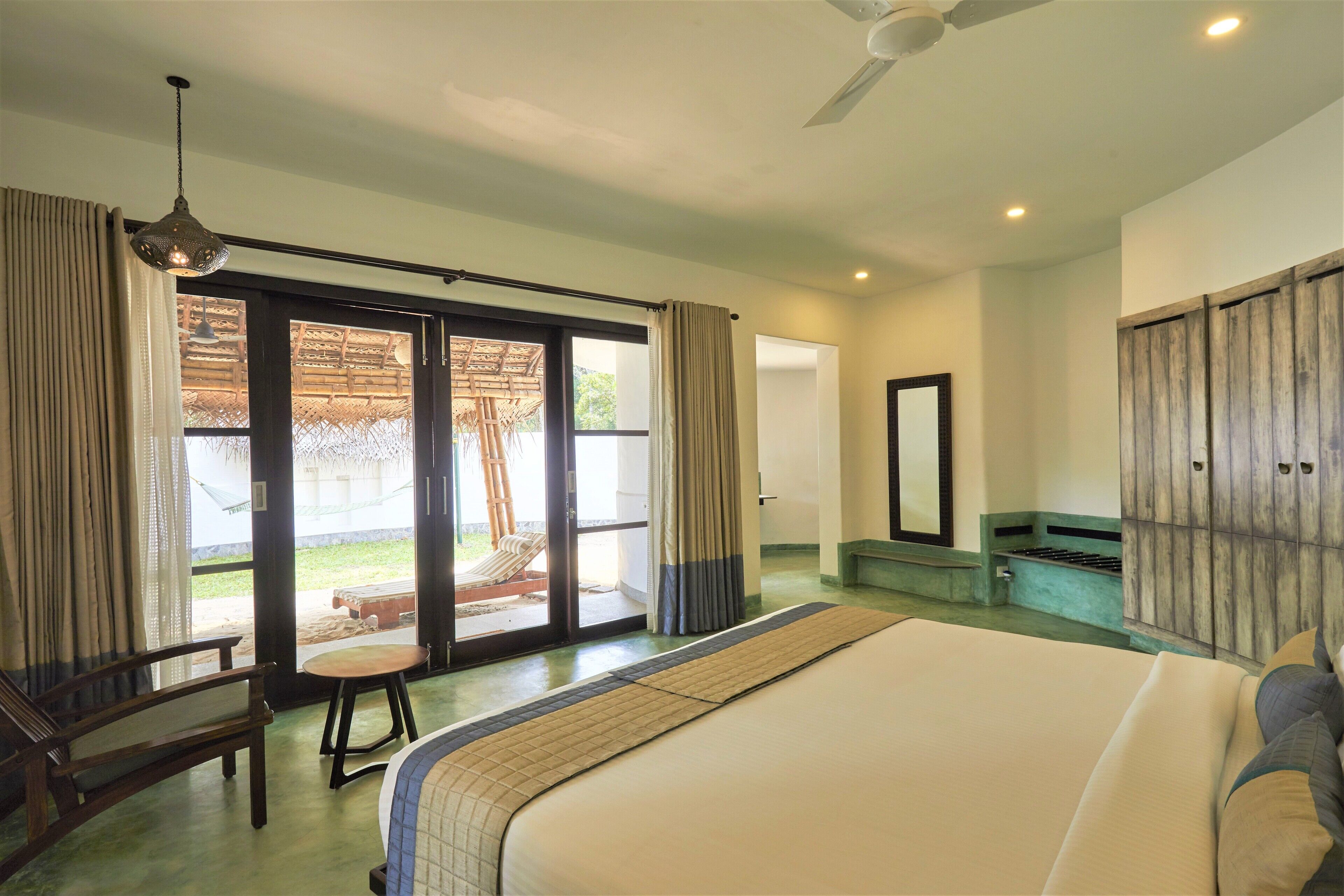A bedroom with a large bed, a wooden wardrobe, a ceiling fan, and a sliding glass door leading to an outdoor area.