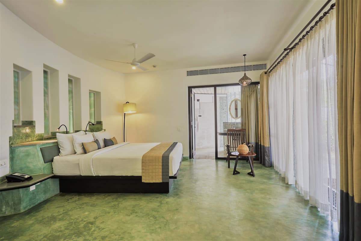 Habitación de hotel con cama, mesita de noche, lámpara y vistas al exterior.