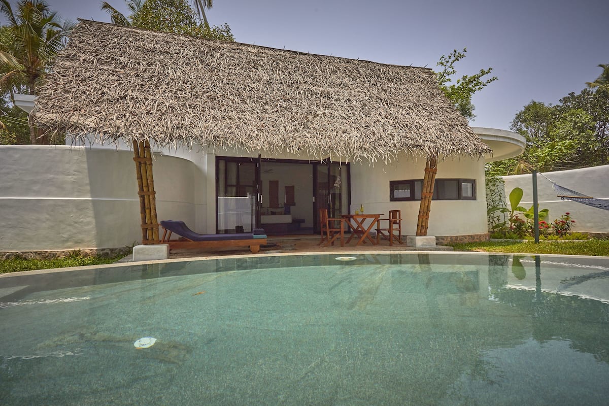 Zona junto a la piscina con una estructura de techo de paja, piscina y un área de descanso con sillas y una mesa.