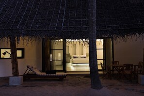 A beachside room with a thatched roof, a bed, a lounge chair, and a dining area. - Xandari Pearl (Cherthala)