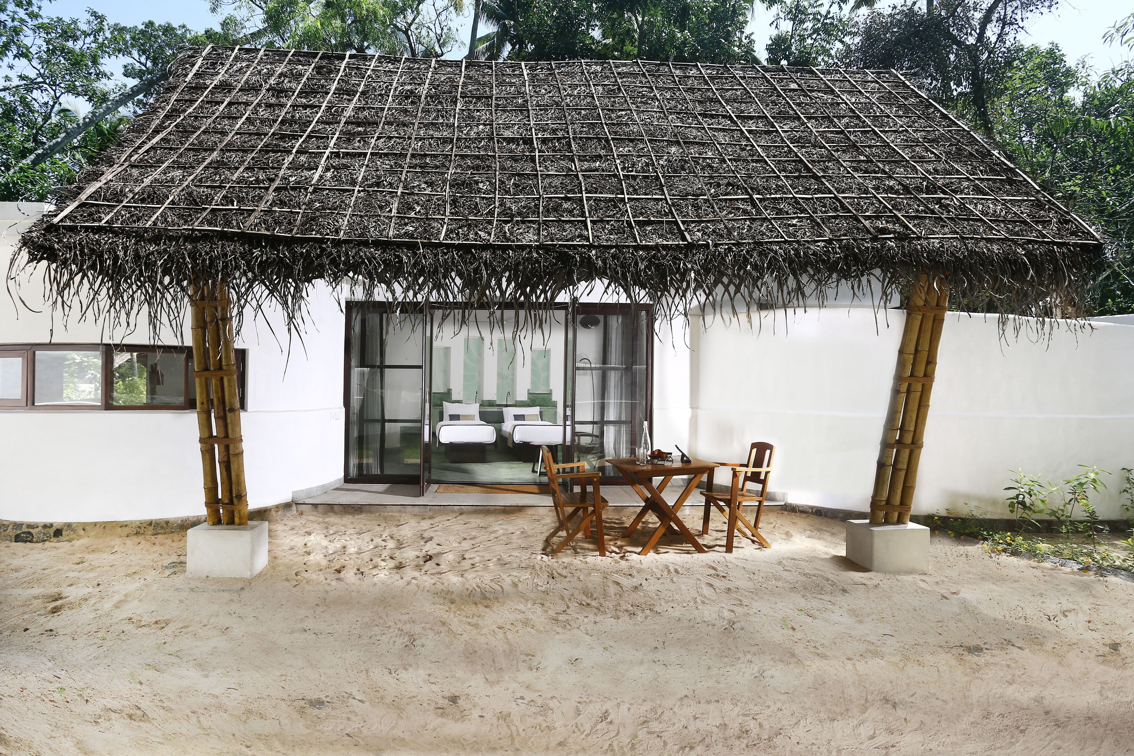 Una estructura con techo de paja, una mesa, sillas, una puerta de cristal y una pared blanca.