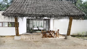 Una estructura con techo de paja, una mesa, sillas, una puerta de cristal y una pared blanca.
