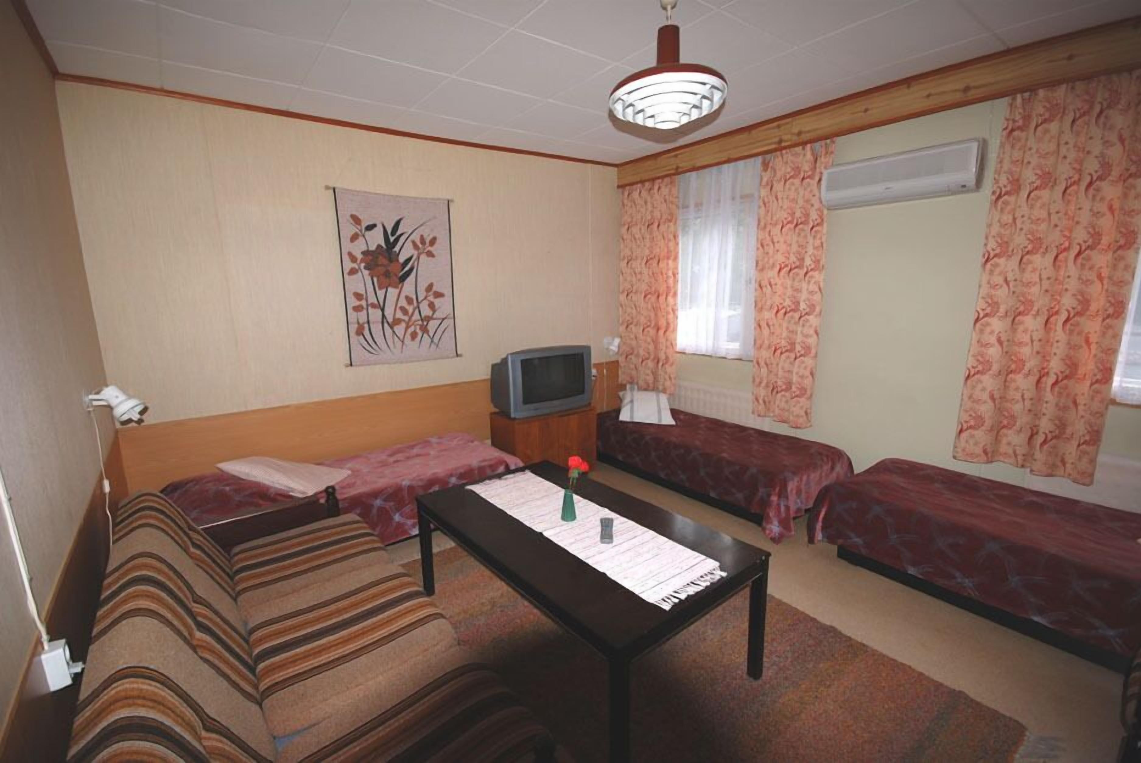 Una habitación con dos camas individuales, una mesita, un televisor y un cuadro con motivos florales en la pared.