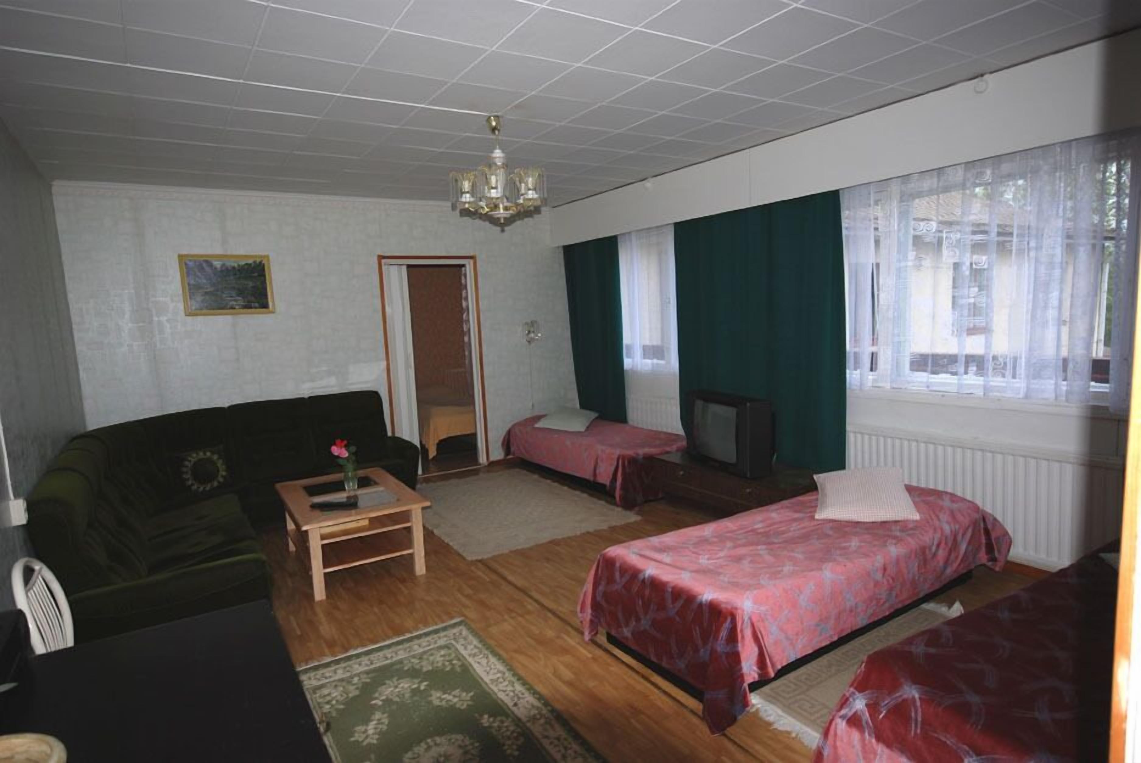 Una habitación con sofá verde, dos camas individuales, una mesa de madera, un televisor y un candelabro.