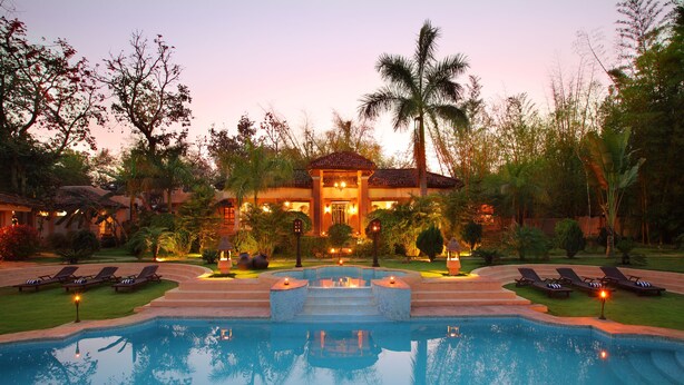A resort with a swimming pool, lounge chairs, and a well-lit building with a tiled roof. - Tuli Tiger Resort (Bichhiya)