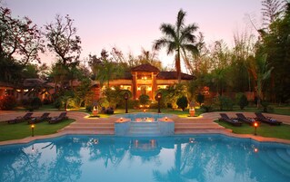 Un resort con piscina, sillas de descanso y un edificio bien iluminado con tejado de tejas.