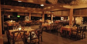 Un restaurante con varias mesas y sillas, vigas de madera en el techo y una iluminación cálida.