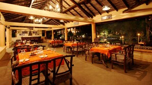 A restaurant with multiple tables and chairs, a high ceiling with wooden beams, and a view of the outdoors. - Tuli Tiger Resort (Bichhiya)
