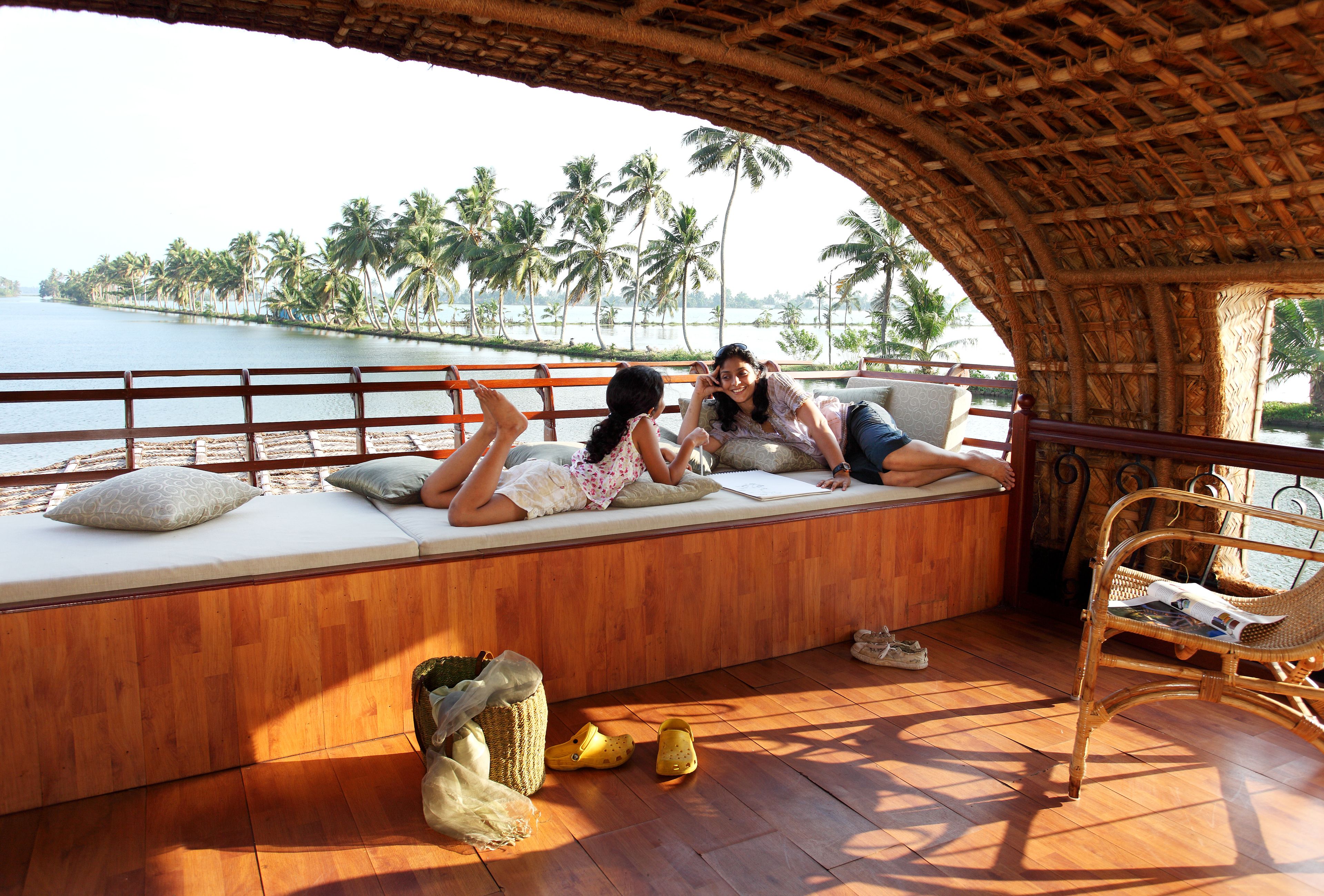 A wooden deck with a thatched roof, a cushioned bench, and a wicker chair.