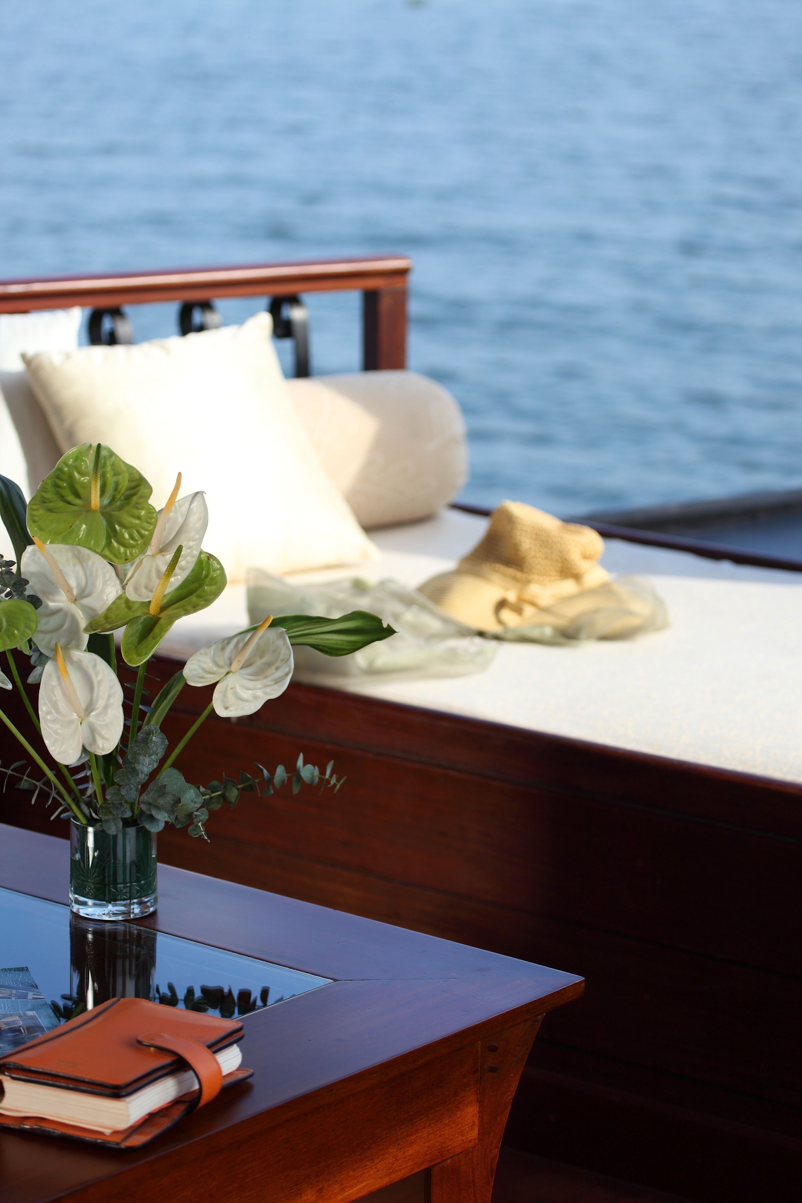 Una cama de madera con almohadas blancas y un sombrero color beige en la cubierta de un barco.