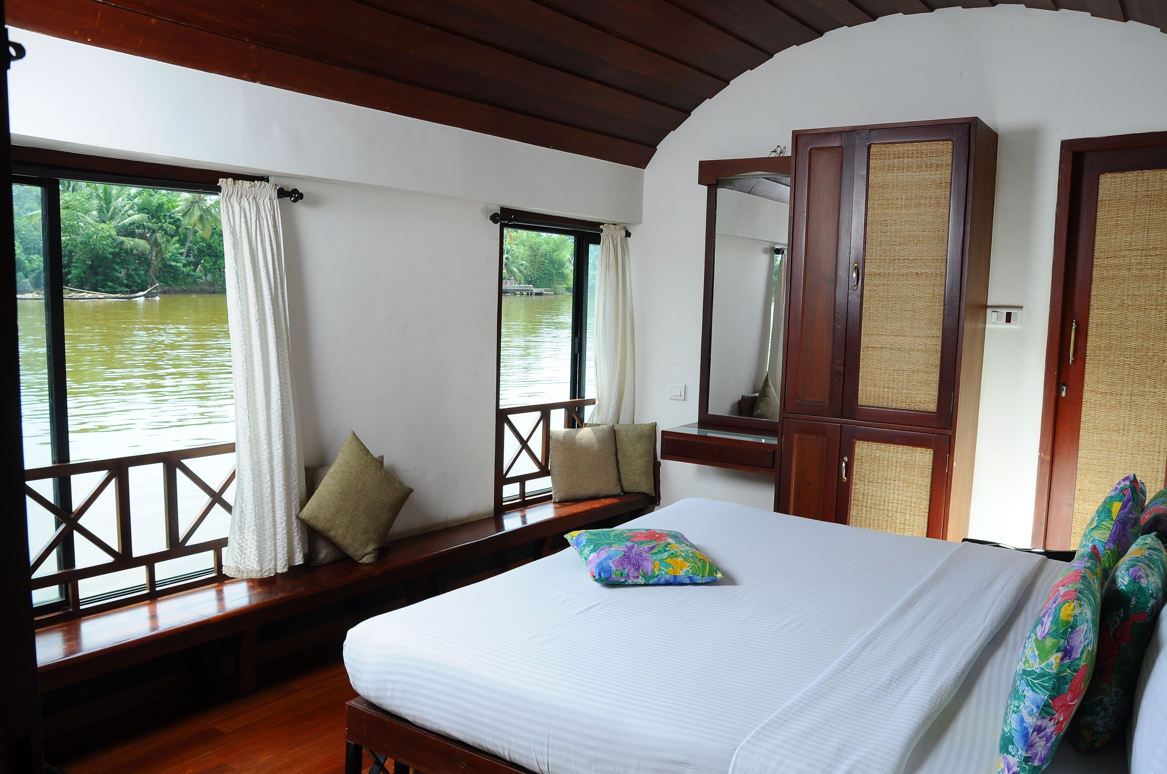 Quarto com cama, um banco junto à janela e vista para a água.