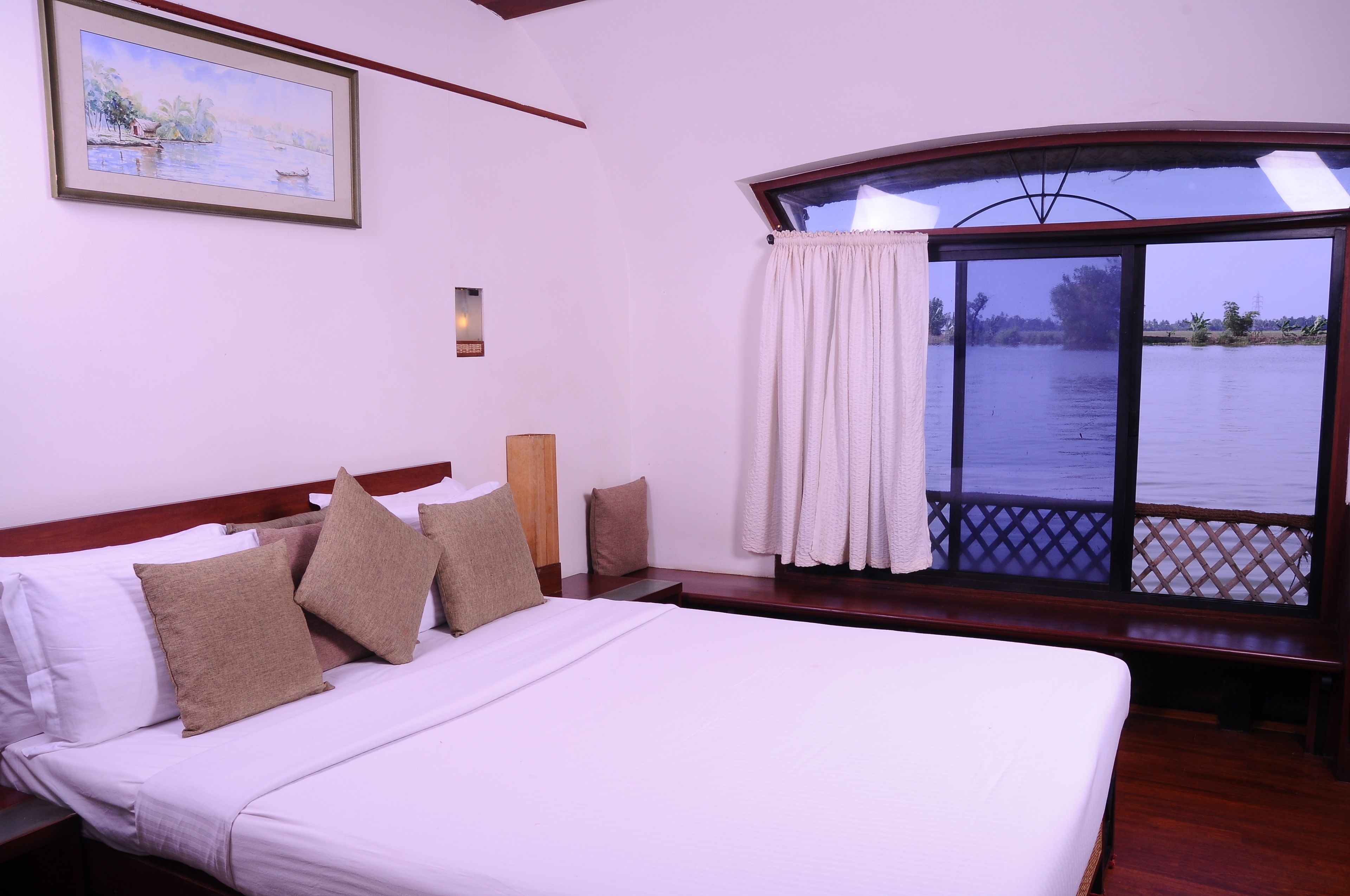 A hotel room with a large bed, a window with a view of a body of water, and a painting on the wall.