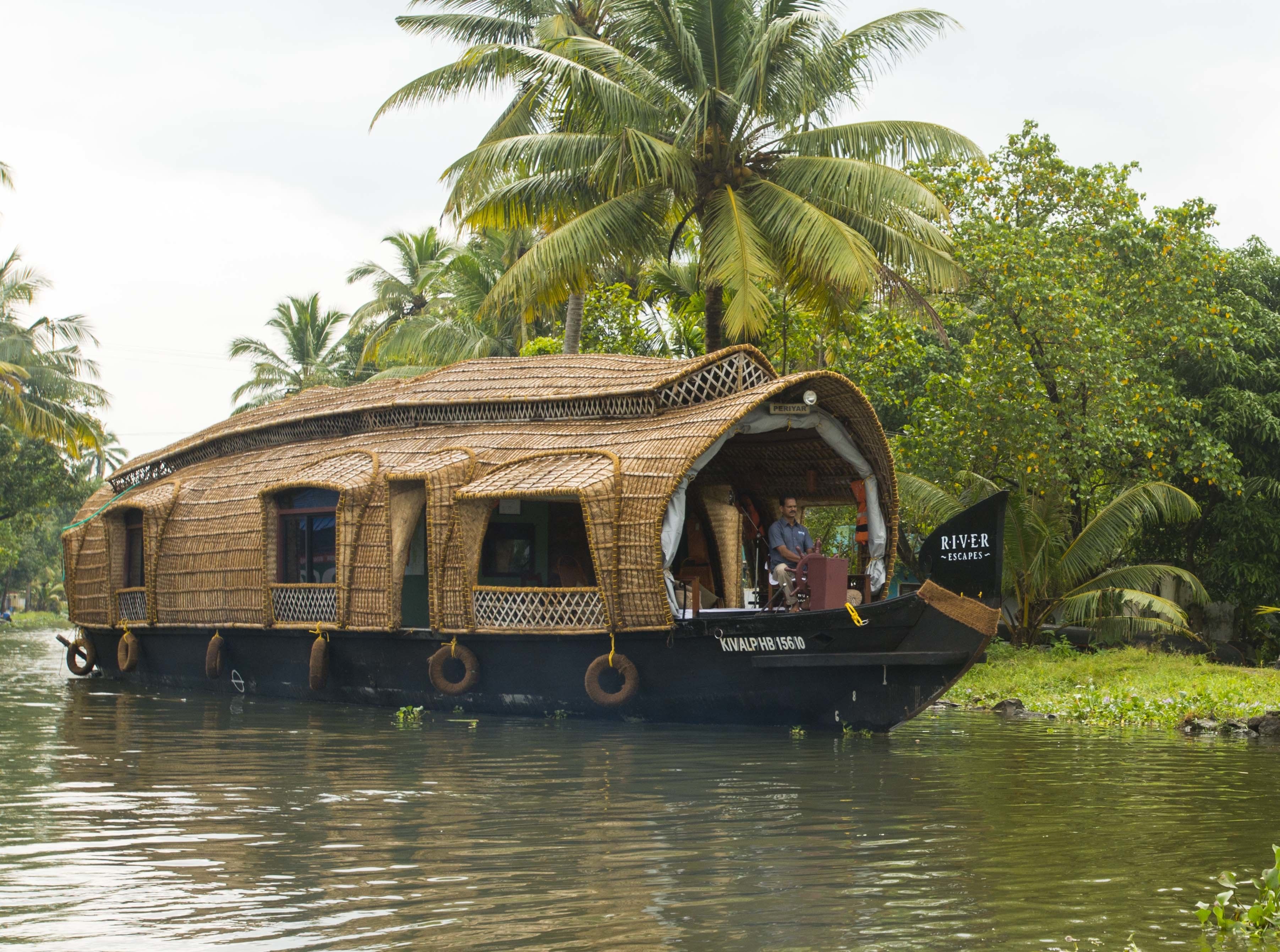 Una casa flotante tradicional con techo de paja, timón y un letrero que dice 'RIVER ESCAPES'.