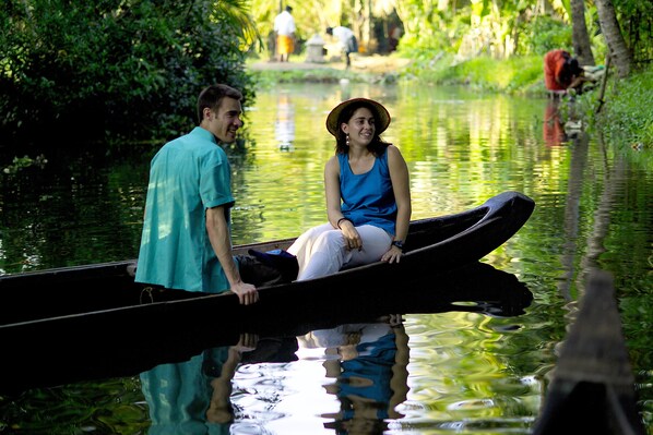 Una pareja en un barco estrecho navegando por un río tranquilo, rodeada de abundante vegetación.