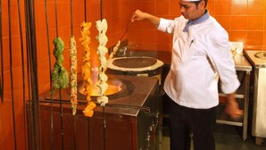 A chef preparing skewers on a grill in a kitchen with orange tiled walls. - Tuli Tiger Corridor (Kurai)