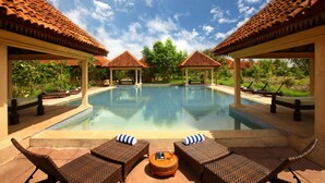 A pool area with lounge chairs and umbrellas, surrounded by covered structures with tiled roofs. - Tuli Tiger Corridor (Kurai)