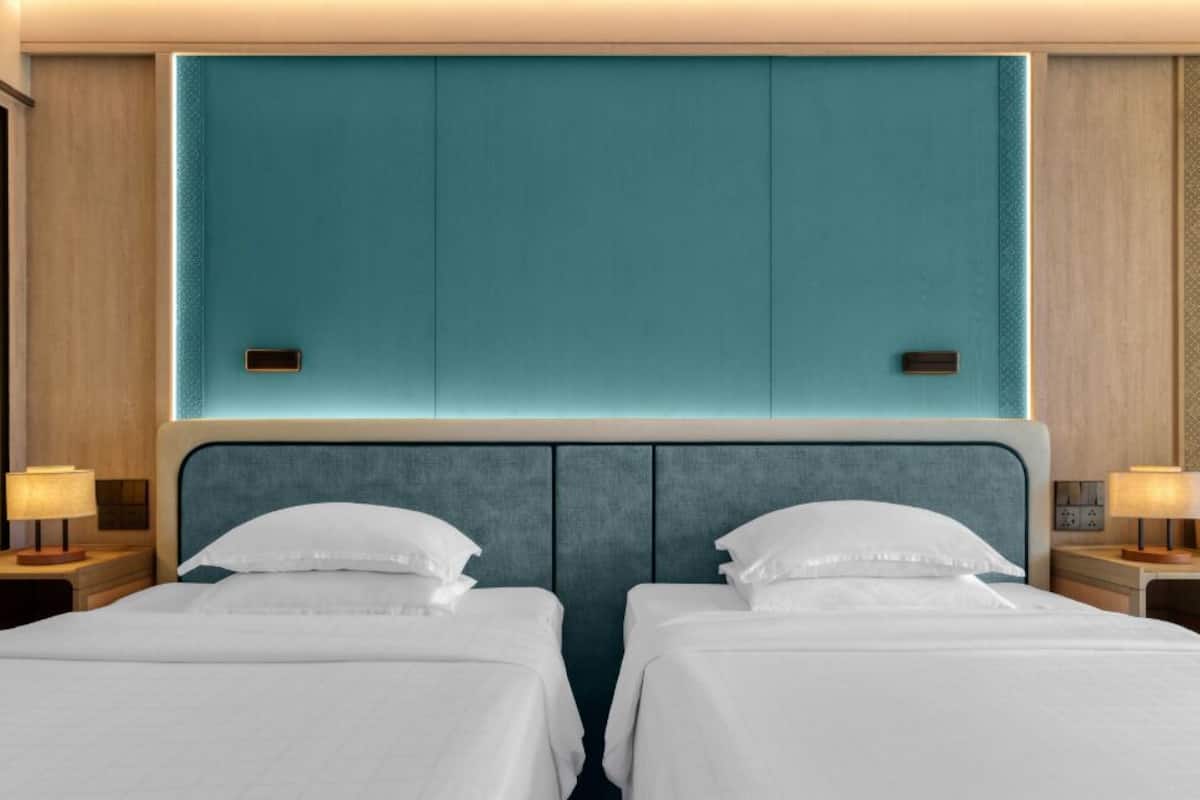 Een hotelkamer met twee bedden, een muur in een blauwgroene tint en bedlampjes.