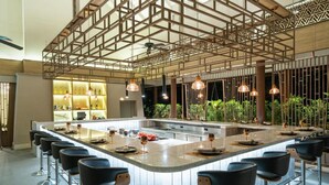 Une cuisine moderne dotée d’un îlot central, de tabourets de bar, de luminaires suspendus et offrant une vue sur la verdure environnante.