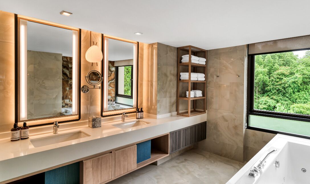 Un baño moderno con un espejo grande, dos lavamanos, una bañera y vistas a zonas verdes.